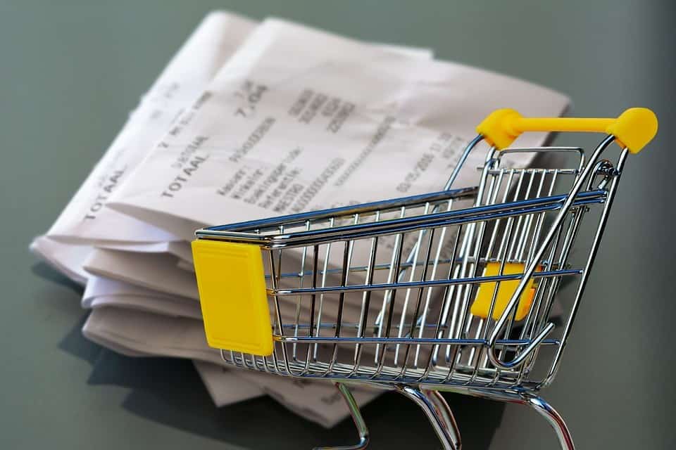 metal shopping cart with yellow handle in front of stack of receipts